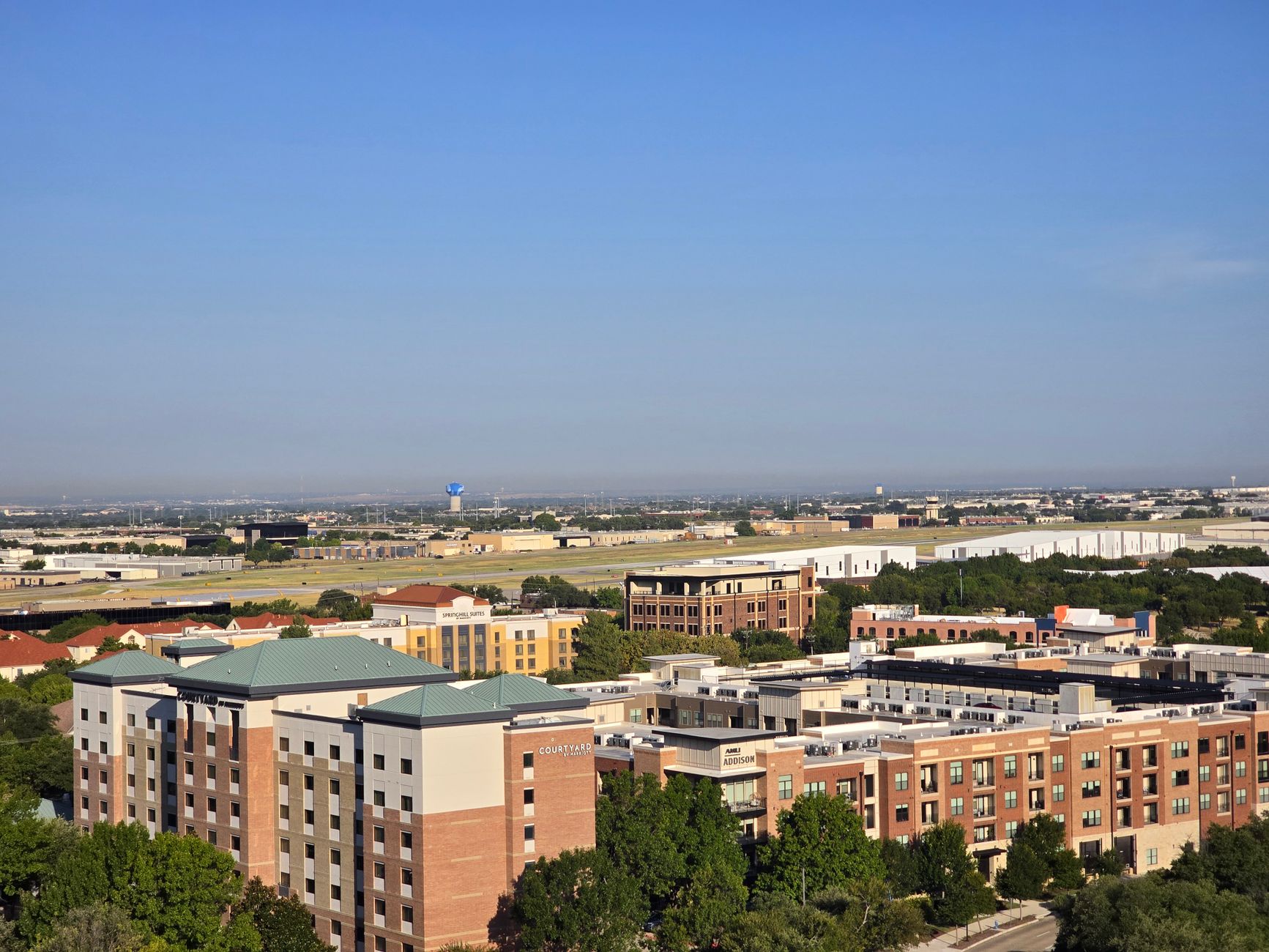 Aerial view of a cityscape with buildings and open spaces under a clear blue sky.