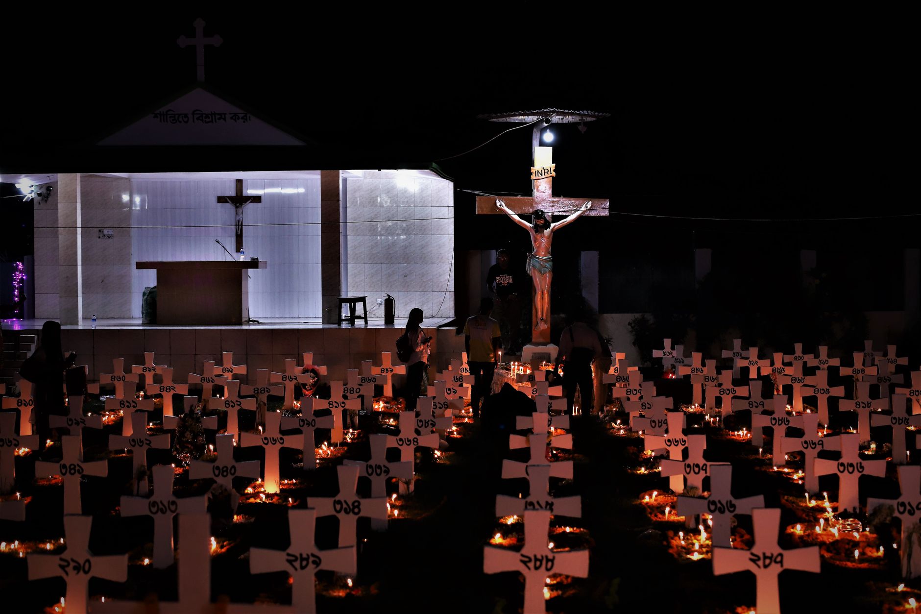 A serene cemetery scene at night, with crosses and candlelit vigils in Dhaka, Bangladesh.